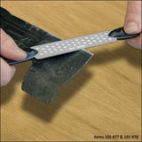 Hands sharpening an axe blade with a diamond sharpening file on a wood surface.