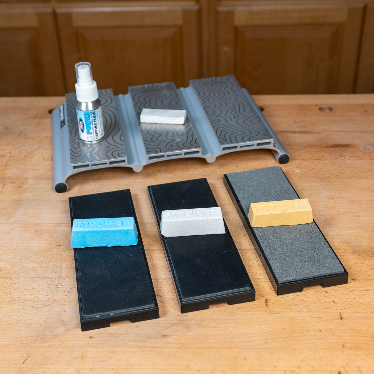 Woodworking sharpening system with three honing stones, abrasive compounds, spray bottle, and base on a workbench.