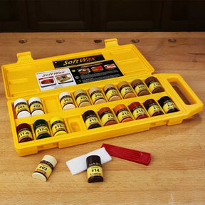 Wood repair wax kit with assorted color sticks, buffer pad, and applicator in a yellow case on a workbench.