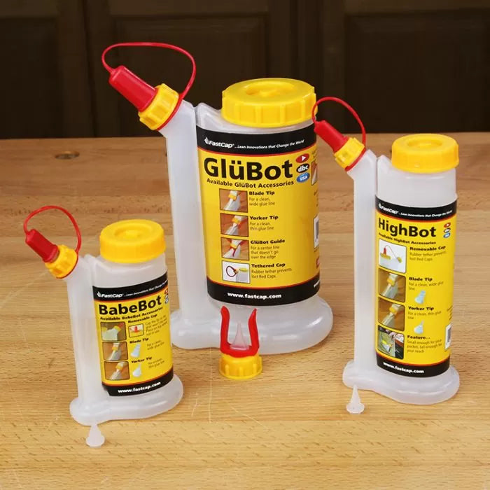 Three woodworking glue bottles with yellow labels and angled red caps on a wooden surface.