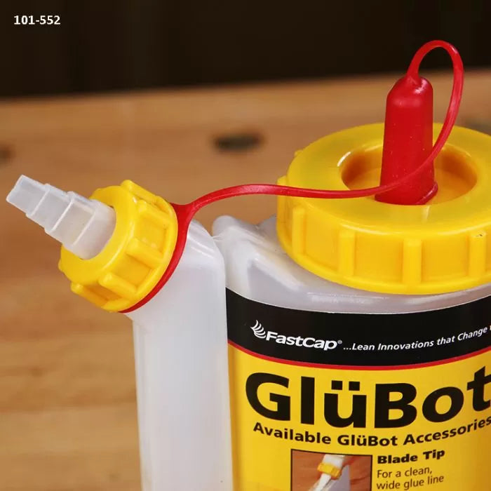 Close-up of GlüBot glue bottle with yellow lid and angled nozzle on a wooden workbench.