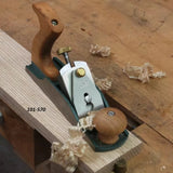 Bench plane labeled 101-570 smoothing wood on workbench with wood shavings