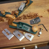 Woodworking hand plane with disassembled parts on workbench, showing handles and metal blades.