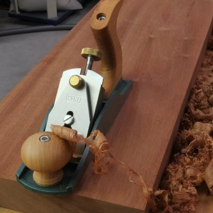 Hand planer shaving wood on a workbench with fresh wood shavings