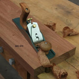 No. 4 bench hand plane smoothing wood on workbench, wood shavings visible, labeled 101-571.