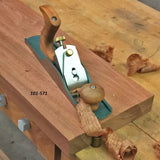 Hand plane smoothing wood on a workbench with wood shavings, labeled 101-571