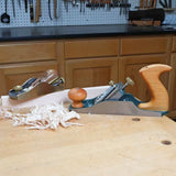 Woodworking hand planes with wood shavings on a workshop bench, tools in background.