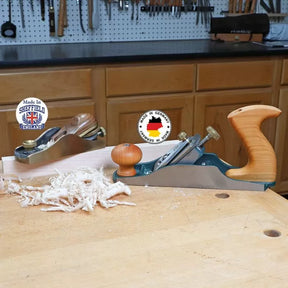 Two woodworking hand planes with wood shavings on a workbench in a workshop setting.