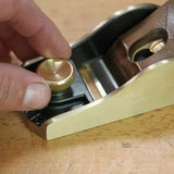 Hand adjusting brass knob on woodworking block plane on workbench