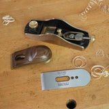 Disassembled woodworking hand plane with brass, wood, and metal parts on a workbench