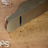 Close-up of brass woodworking hand plane on a wood surface with shavings.