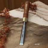 Woodworking chisel with wood handle and brass ferrule on carved wood surface, shavings nearby