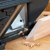 Close-up of jointer planer blade cutting edge with wood shavings and angled wood piece