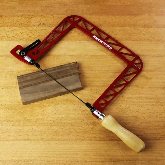 Precision coping saw with red frame and wood handle next to a wooden trim piece on a workbench.