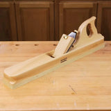 Wooden jointer hand plane on a woodworking bench with cabinet background