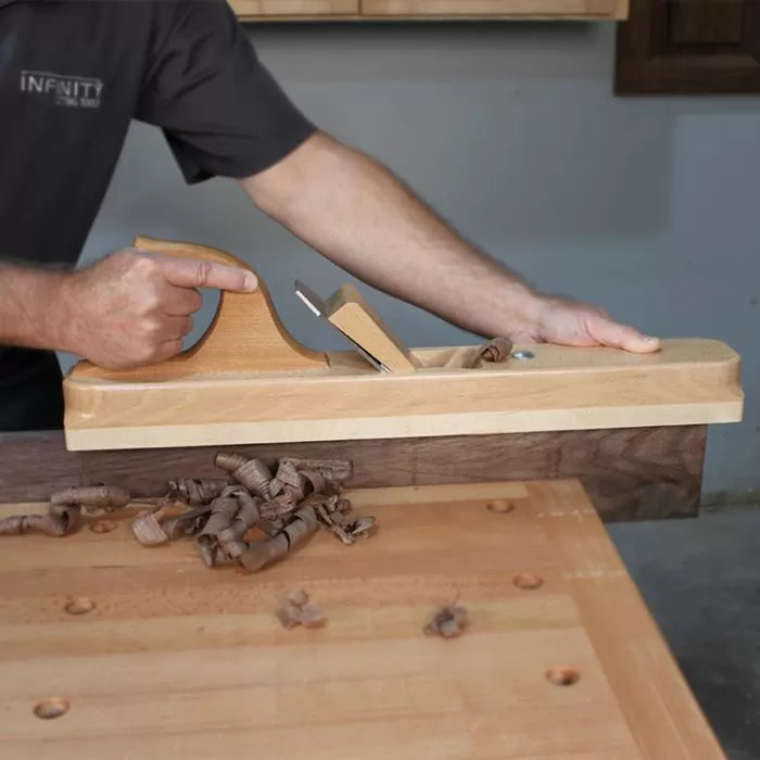 Woodworker using a wooden jointer hand plane to smooth hardwood edge on workbench.