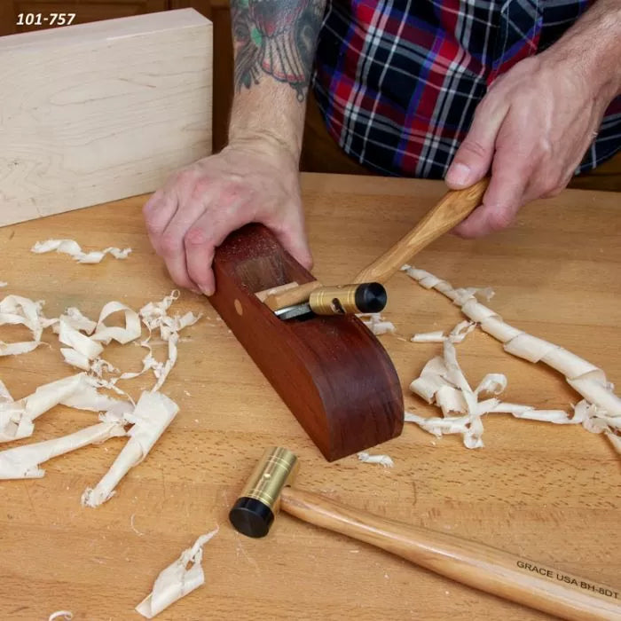 Hand planing wood with a woodworking hand plane, brass hammer, and wood shavings on workbench