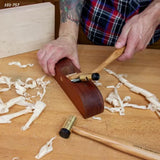 Hand planing wood with a woodworking hand plane, brass hammer, and wood shavings on workbench