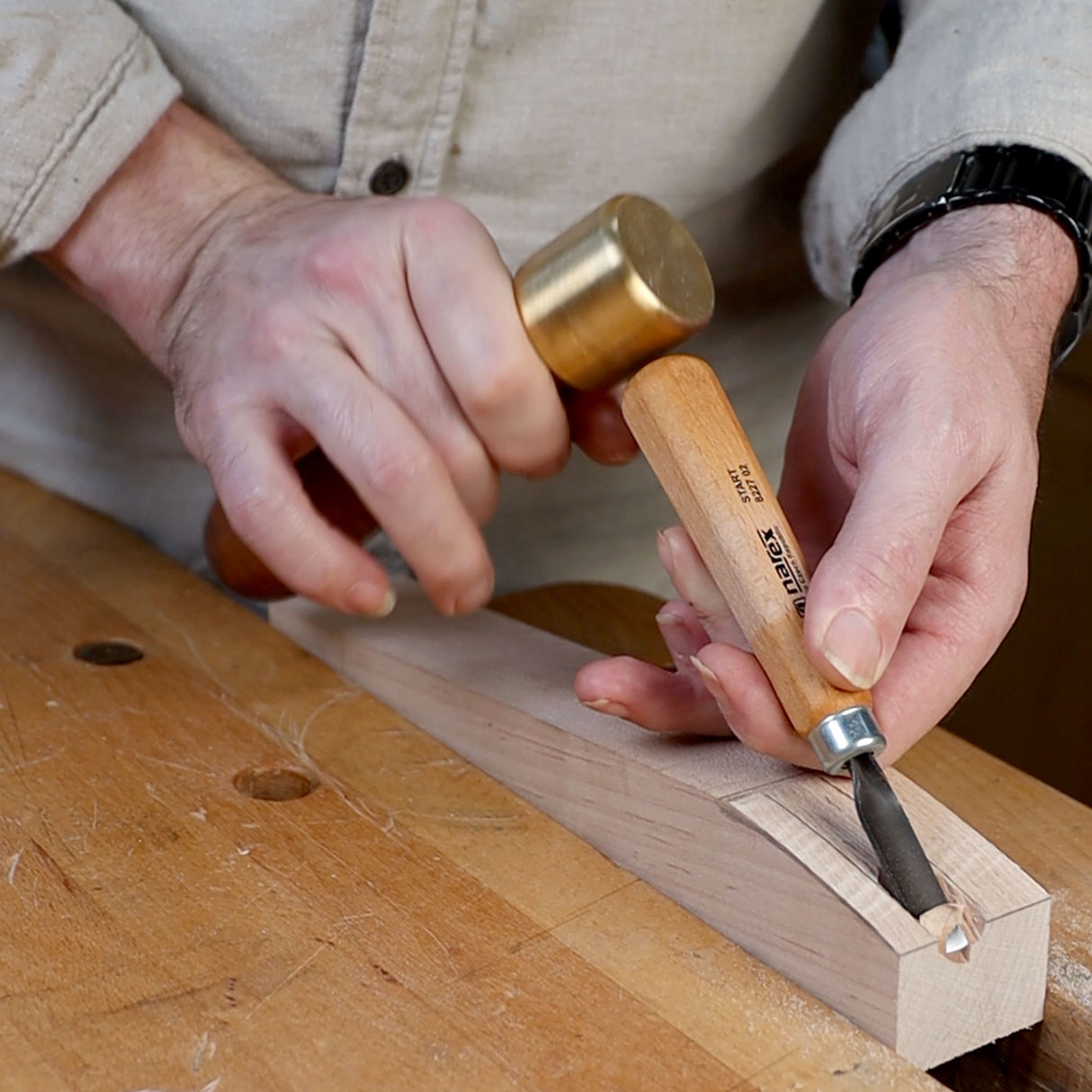Woodworker using brass mallet and chisel to carve mortise in hardwood block