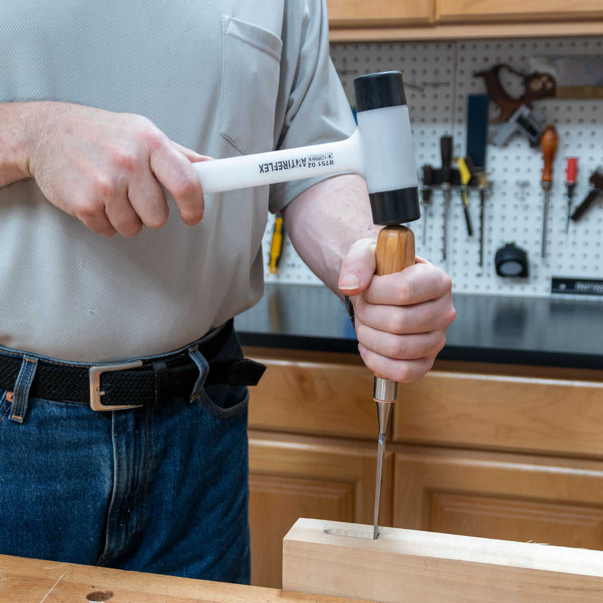 Woodworker using a dead blow mallet and chisel on a wooden board in a workshop.