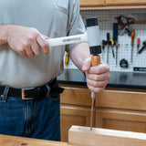 Woodworker using a dead blow mallet and chisel on a wooden board in a workshop.
