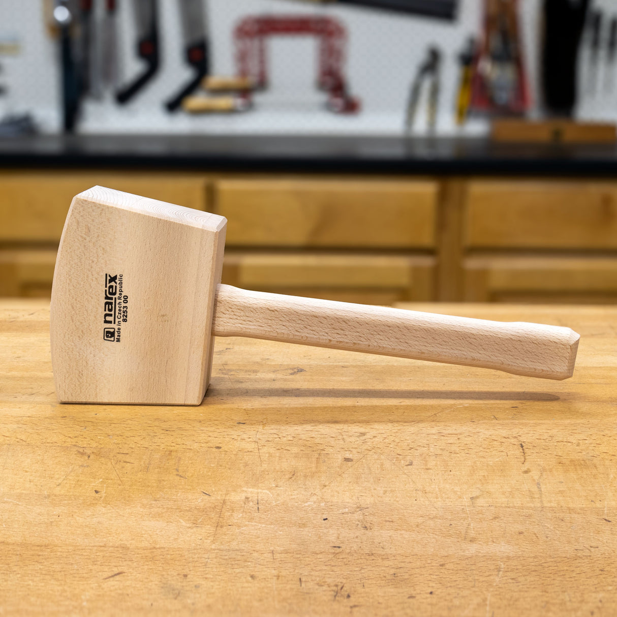 Wooden heavy bench mallet with square head and long handle on a workbench in a workshop