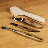Three wood carving tools with wooden handles and a carved wooden spoon blank on a wood surface