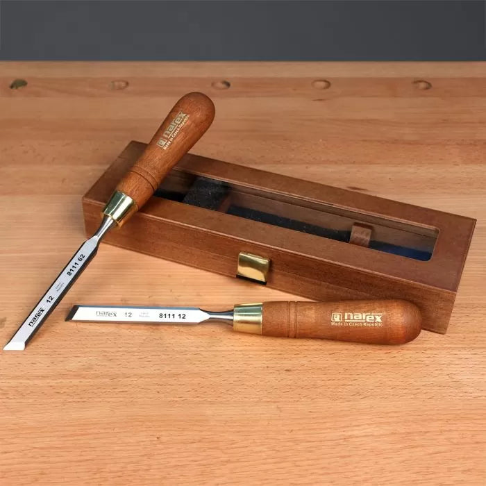 Woodworking chisels with wooden handles and brass ferrules on a wooden workbench, next to a wooden storage box.