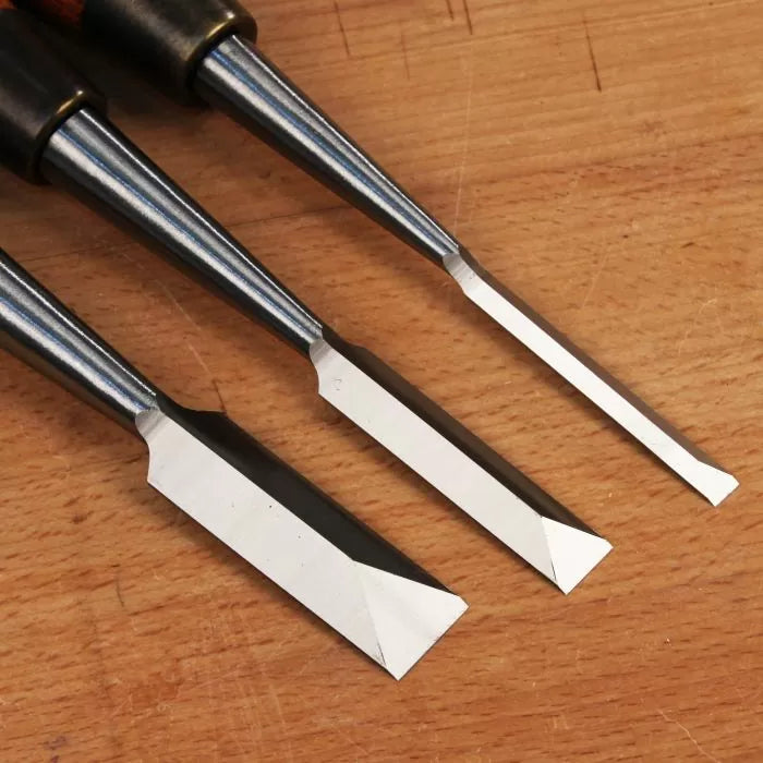 Set of three woodworking chisels with sharp beveled edges on a wooden surface