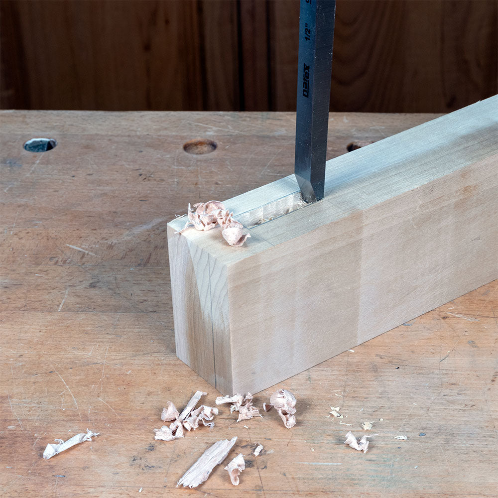 Chisel cutting mortise in hardwood block on woodworking bench with wood shavings