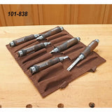 Set of six woodworking chisels with wooden handles in a brown tool roll on a workbench.