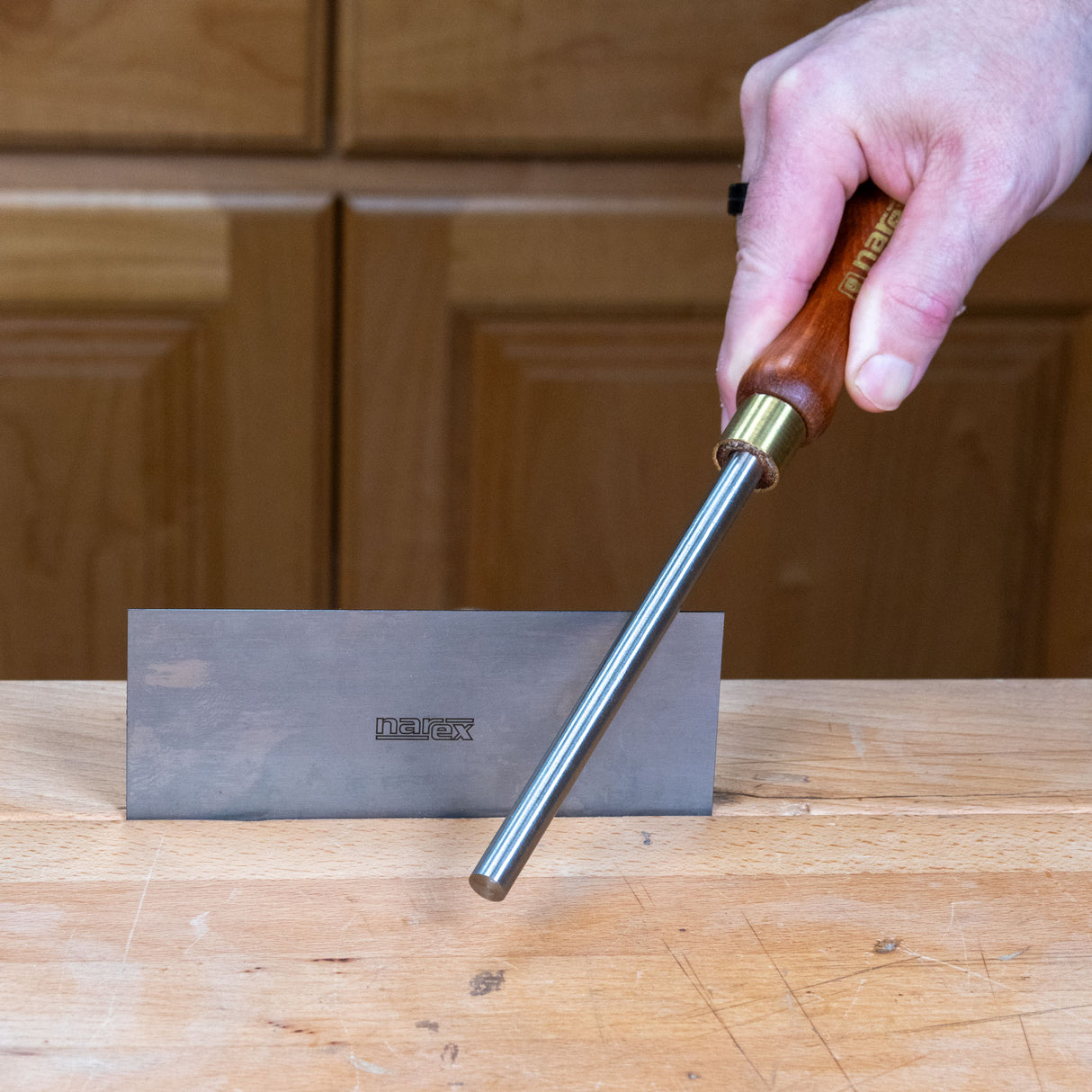 Woodworker using the Narex burnisher to hone a scraper edge on a sharpening stone at a workbench
