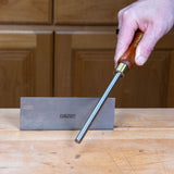 Woodworker using the Narex burnisher to hone a scraper edge on a sharpening stone at a workbench