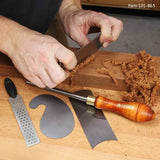 Woodworker using a hand scraper on wood with cabinet scrapers, burnisher, and file nearby.
