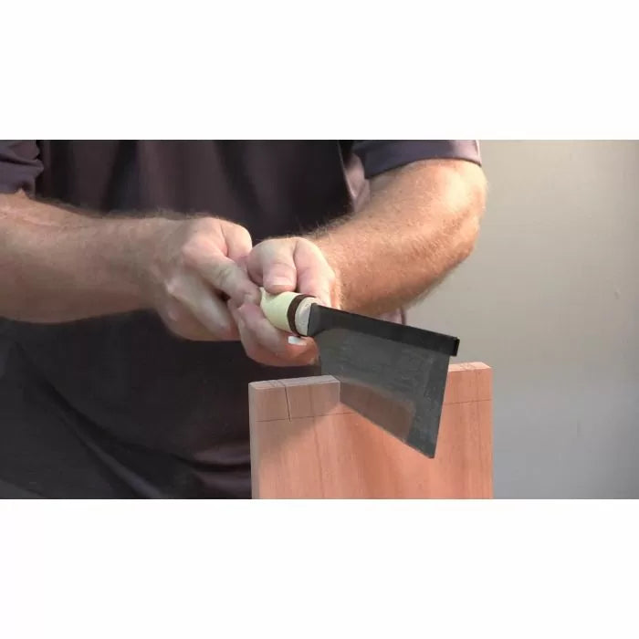 Woodworker using a Japanese dovetail saw to cut precise joints in a wooden board.