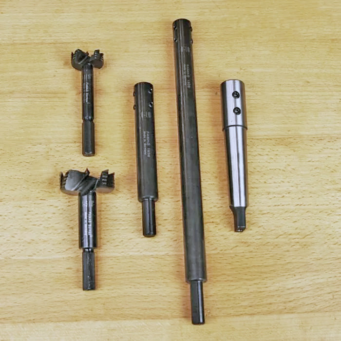 Five woodworking boring bits and extensions on a wood surface, precision cutting tools