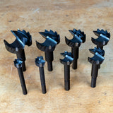 Set of eight Forstner drill bits arranged on a wooden workbench for woodworking