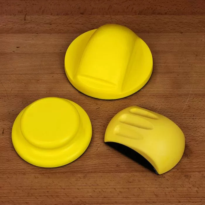 Yellow woodworking sanding blocks set on a wooden surface, ergonomic hand grips visible.