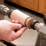 Woodworker sanding a spindle on a wood lathe in a workshop setting