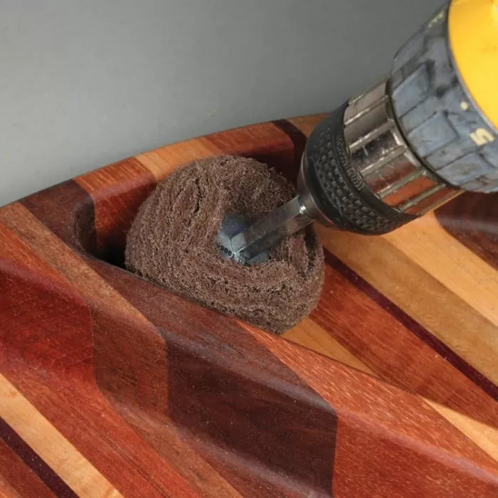Drill with abrasive accessory sanding concave groove in striped wooden board
