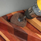 Drill with abrasive accessory sanding concave groove in striped wooden board