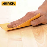 Hand sanding wood surface with yellow sandpaper sheet, Mirka logo visible, woodworking tool