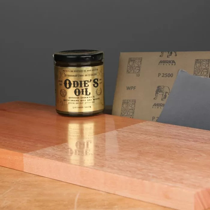 Odie's Oil wood finish jar with sandpaper sheets and polished wood surface for woodworking