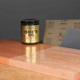 Odie's Oil wood finish jar with sandpaper sheets and polished wood surface for woodworking