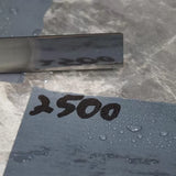 2500 grit wet sandpaper sheet with water droplets and a reflective metal blade