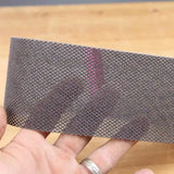 Hand holding mesh abrasive sanding strip over wood surface, woodworking tool accessory