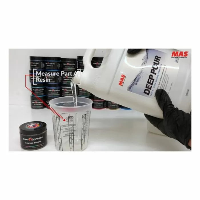 Pouring MAS Deep Pour resin into a measuring cup with containers in the background, woodworking supplies.