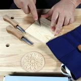 Woodworker carving floral pattern into wood block with hand carving tools on a workbench