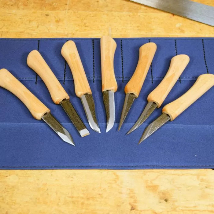 Set of seven wood carving knives with wooden handles on a blue tool roll, woodworking tools.