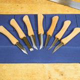 Set of seven wood carving knives with wooden handles on a blue tool roll, woodworking tools.